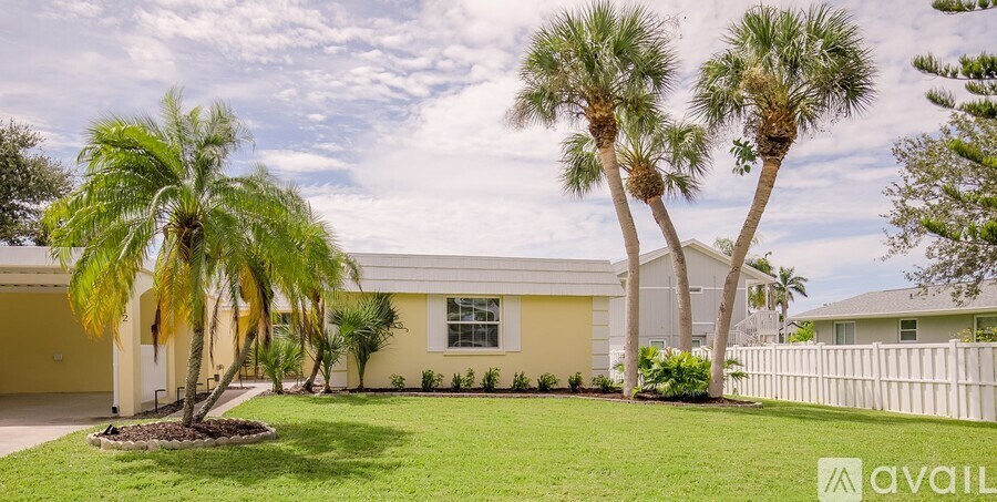 A house with a white fence and palm trees in front.