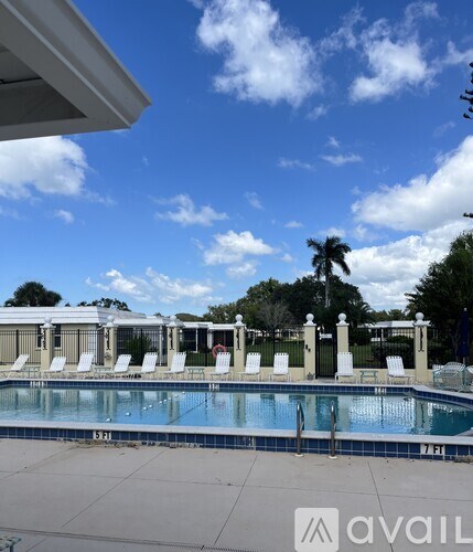A pool with chairs and a fence in the background.