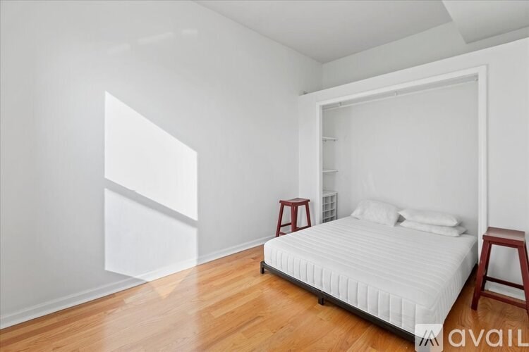 A white bedroom with a bed, pillows, and a wooden floor.