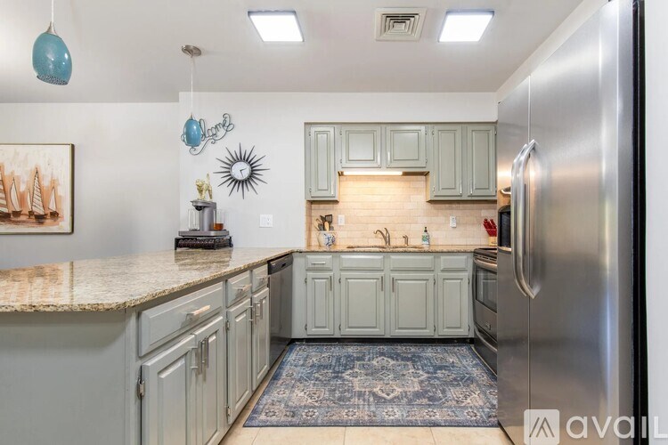 A kitchen with a refrigerator, cabinets, and a rug.