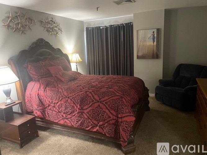 A bedroom with a red bedspread and a black chair.