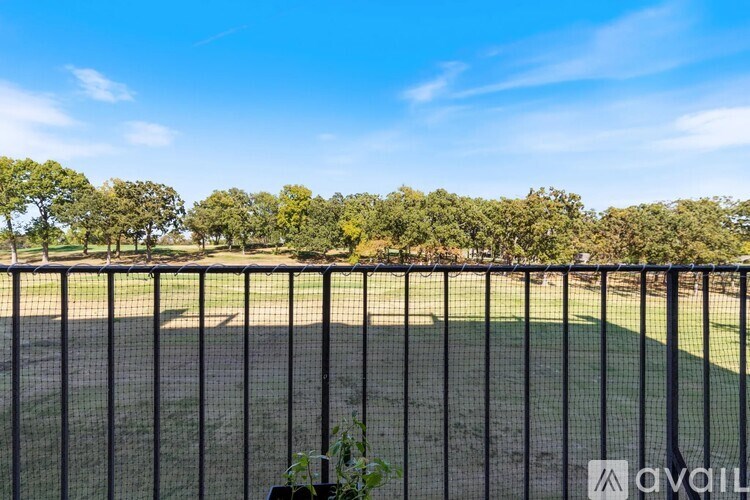 A tennis court is surrounded by a black fence and trees.