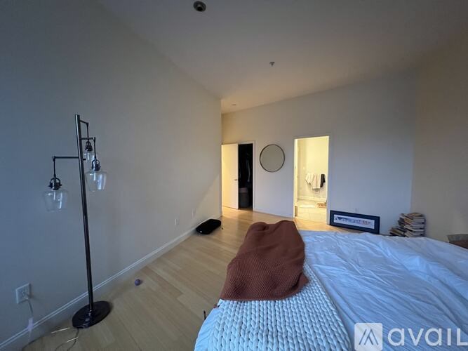 A bedroom with a bed, a floor lamp, and a brown hat on the bed.