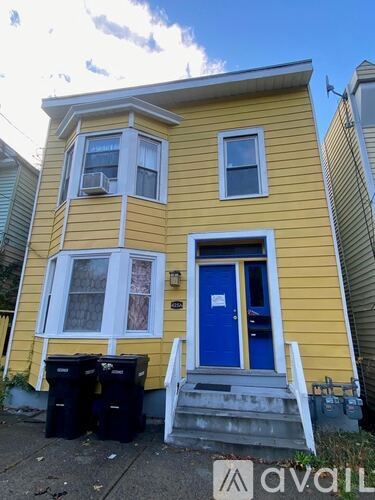 A yellow house with a blue door and two trash bins in front.