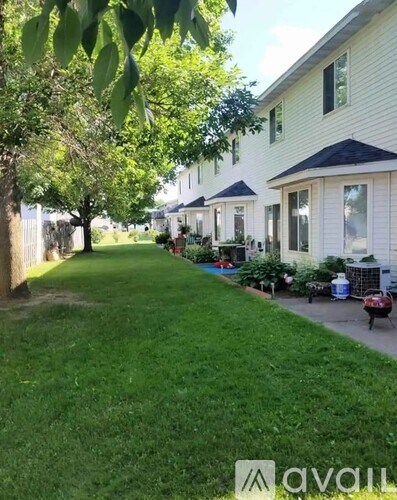 A grassy area in front of a white house with a tree on the left.