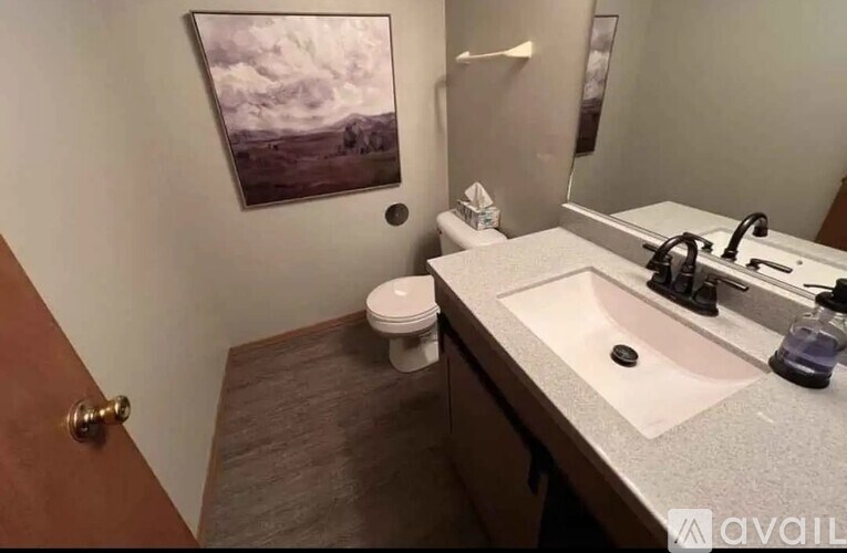 A bathroom with a toilet, sink, and a painting on the wall.