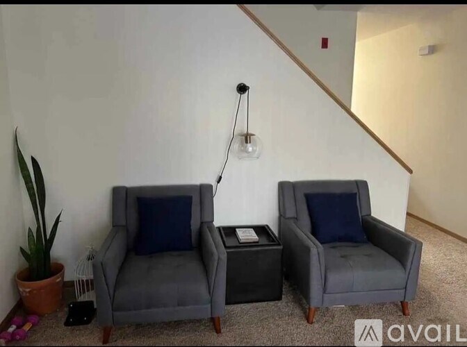 Two grey chairs with blue pillows are in a room with a plant and a hanging light fixture.