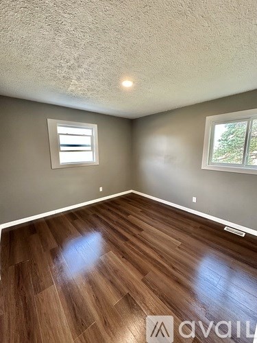 A room with wooden flooring and two windows.