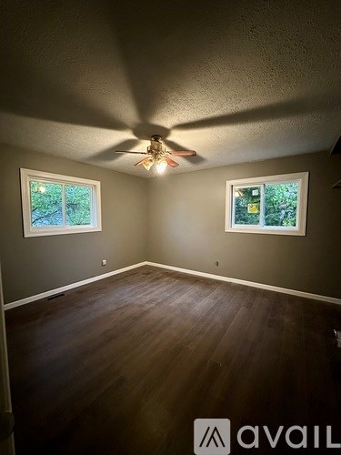 A room with a ceiling fan and two windows.