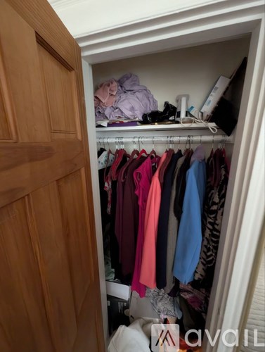 A closet with clothes hanging and a white shelf with items on it.