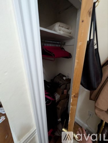 A small closet with a white door is full of clothes.