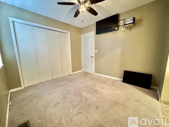 A room with a ceiling fan and a flat screen TV mounted on the wall.