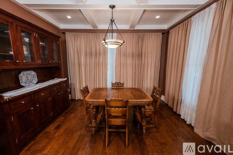 A wooden dining table with chairs is set in a room with curtains.