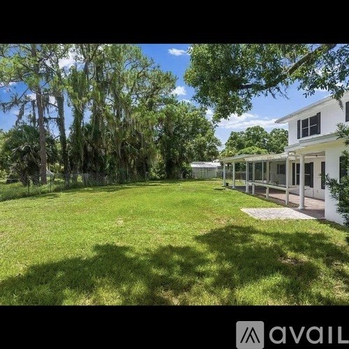 A white house with a large yard and trees in the background.