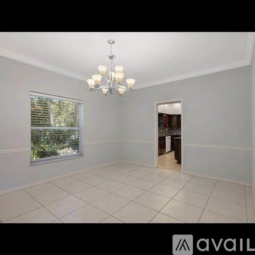 A room with a chandelier, a window with blinds, and a door leading to another room.