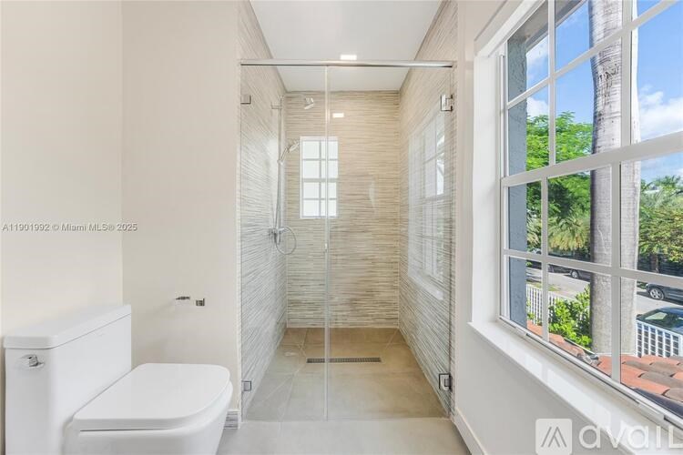 A bathroom with a toilet, a walk-in shower, and a window overlooking a tree.