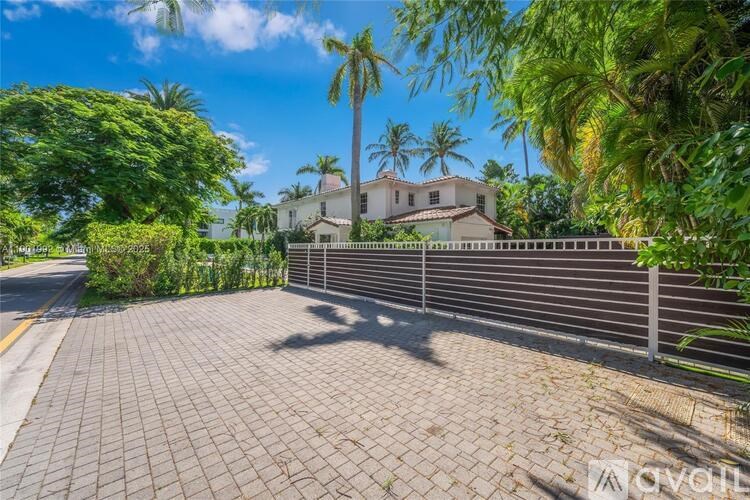 A house with a driveway and a fence is surrounded by greenery.