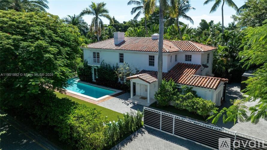 A white house with a red tile roof is surrounded by greenery.