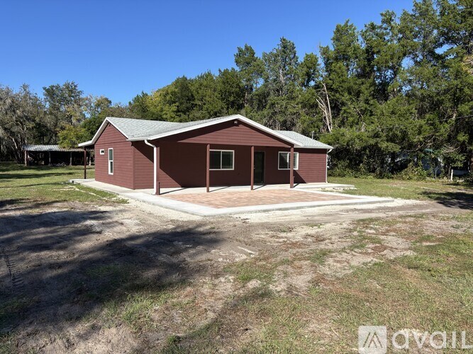 A small red house with a grey roof is surrounded by trees and grass.