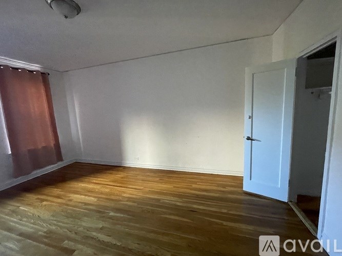 A room with wooden flooring and white walls, with a door on the right side.