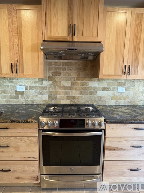 A stainless steel oven with a black glass door is in a kitchen with wooden cabinets.