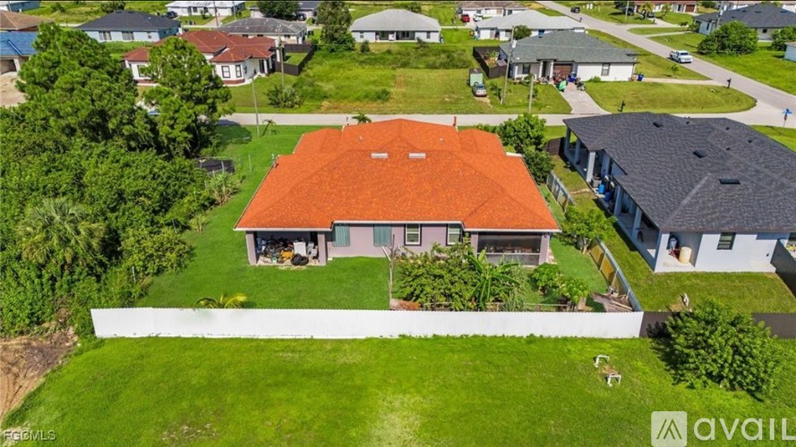 A house with a red roof is surrounded by other houses and greenery.