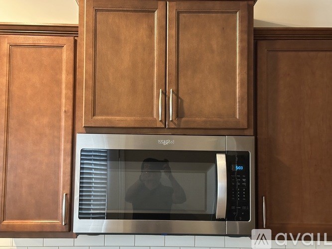A stainless steel microwave oven with a digital display and control panel is installed in a kitchen with wooden cabinets.
