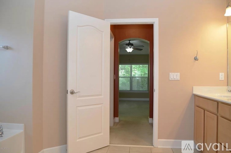 A white door is open to a room with a ceiling fan and a window.