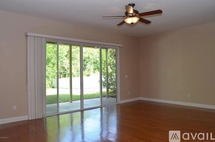 A room with a ceiling fan and sliding glass doors leading to a green outdoor area.