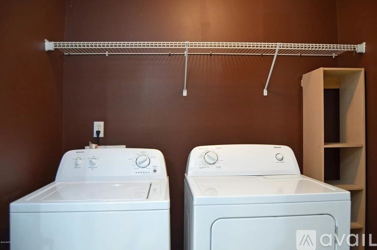 Two washing machines are sitting under a clothes drying rack.