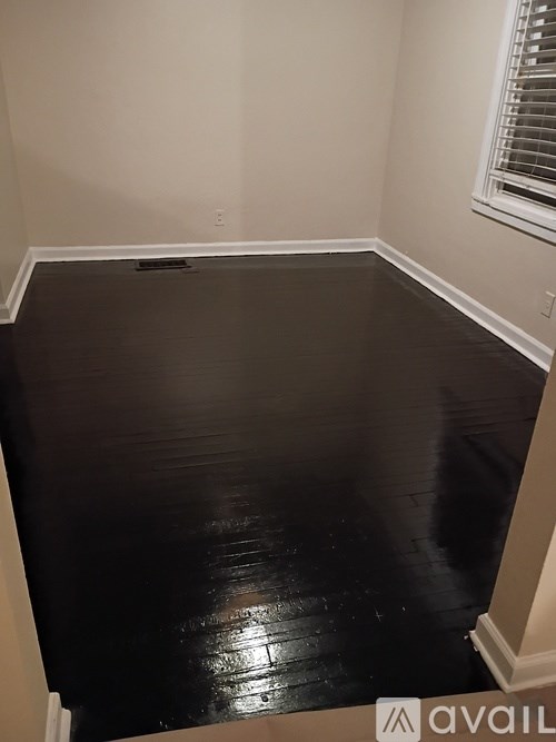A room with a black floor and a window with blinds.