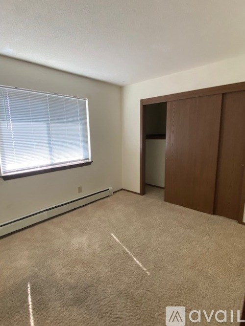 A room with a carpeted floor, a window with blinds, and a wooden door.