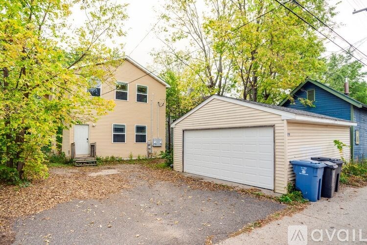 A house with a blue garage door is surrounded by trees and has a gravel driveway.