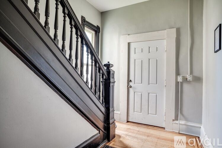 A white door is in a hallway with a wooden staircase.