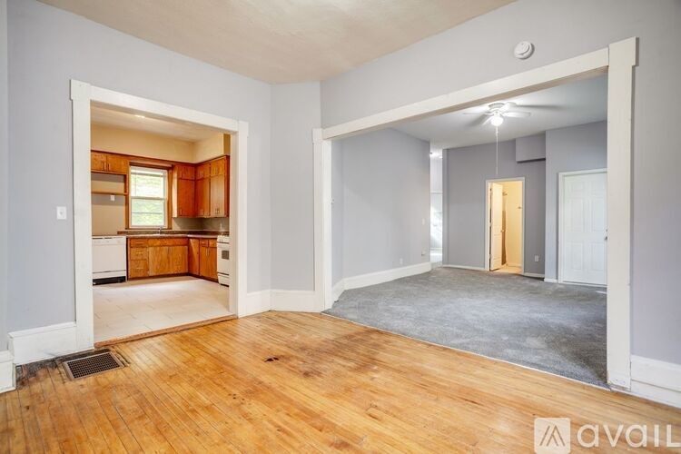A room with wooden floors and a kitchen visible through the open door.