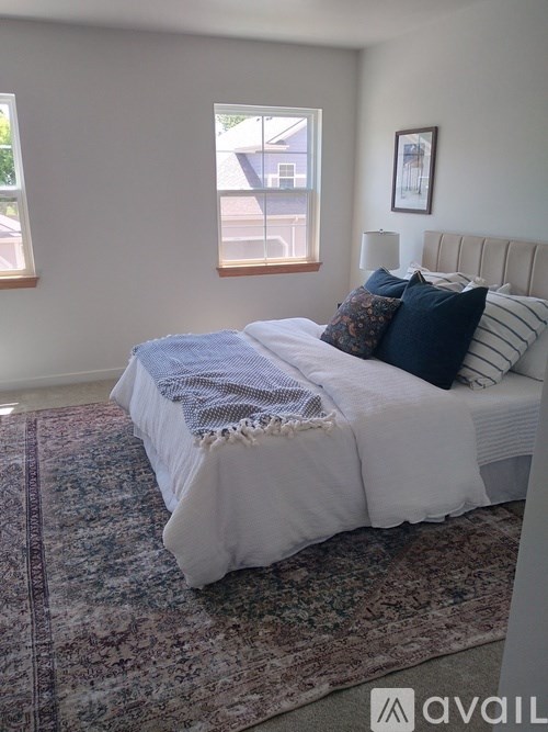 A bed with a white comforter and a blue throw is in a room with a window.