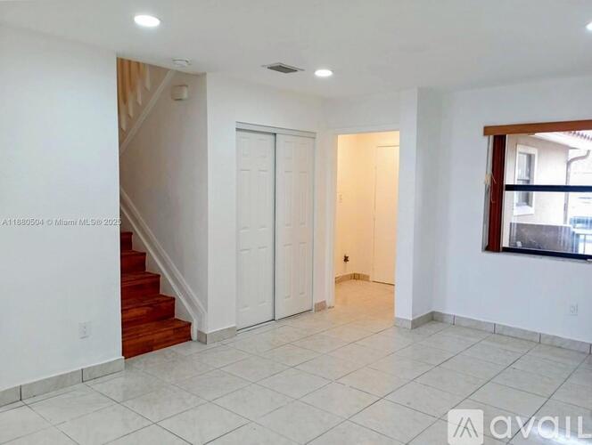 A spacious room with a staircase, two doors, and a window.