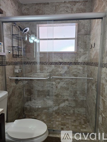 A bathroom with a toilet, a glass shower door, and a window.