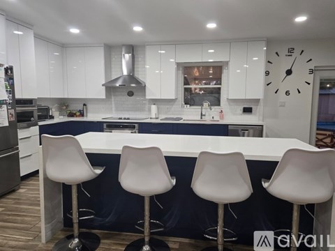 A modern kitchen with white cabinets and a large island with three white barstools.