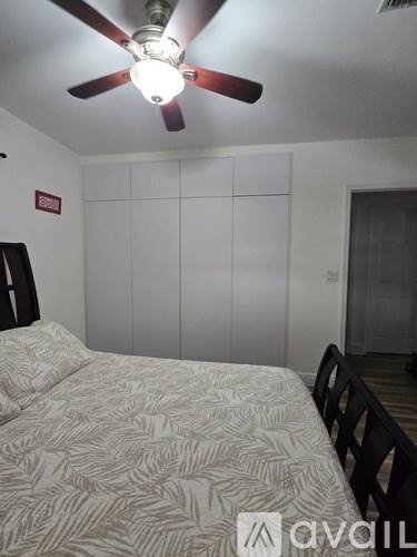 A bedroom with a bed, chair, and ceiling fan.