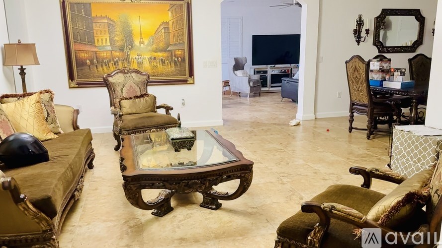 A living room with a large painting on the wall and a variety of furniture including a sofa, armchair, and coffee table.