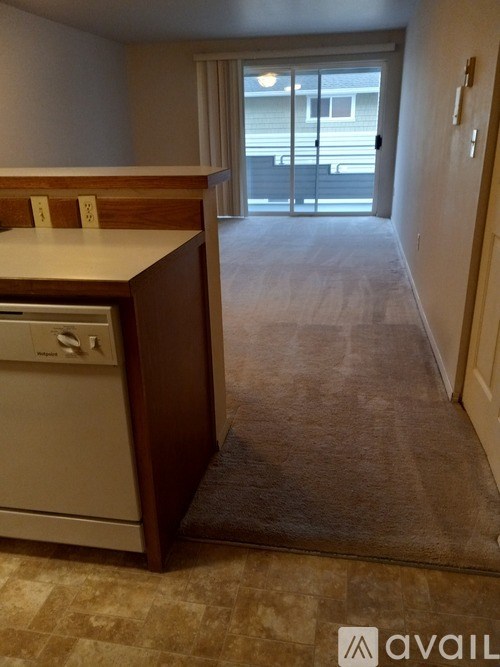 A kitchen with a dishwasher and a carpeted hallway leading to a balcony.