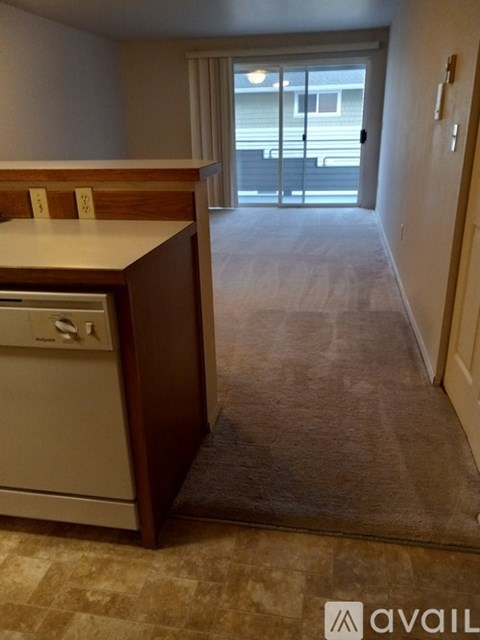 A kitchen with a dishwasher and a carpeted hallway leading to a balcony.