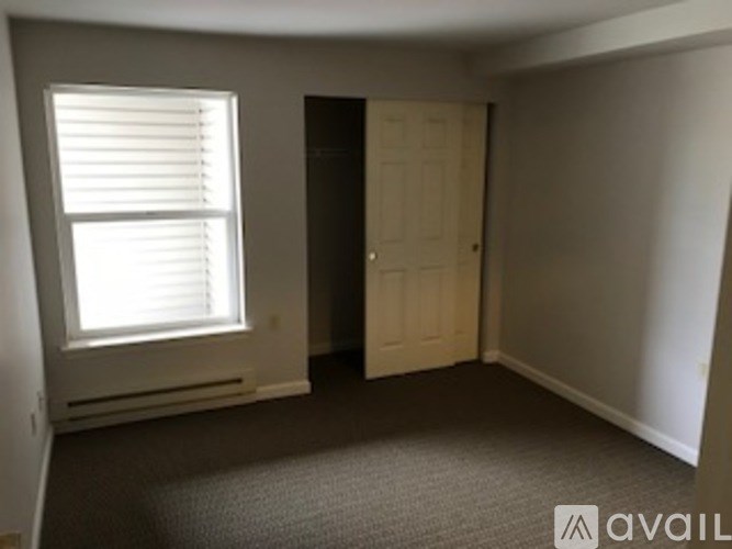 A room with a carpeted floor, a door, and a window with blinds.