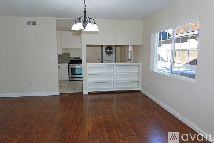 A room with wooden floors and a kitchen area in the background.
