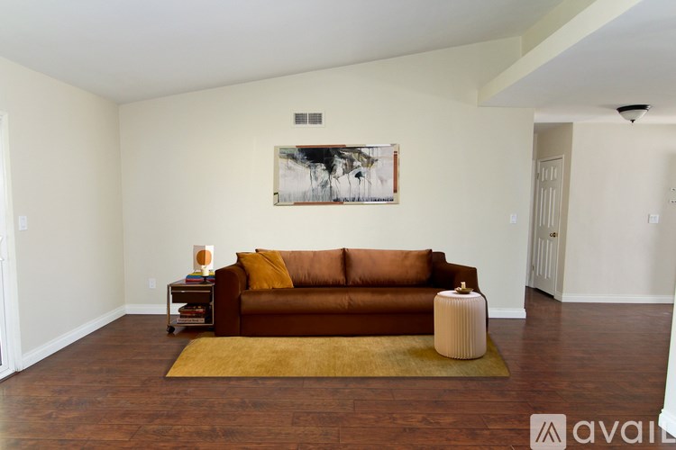 A brown couch sits in a living room with a rug and a picture on the wall.
