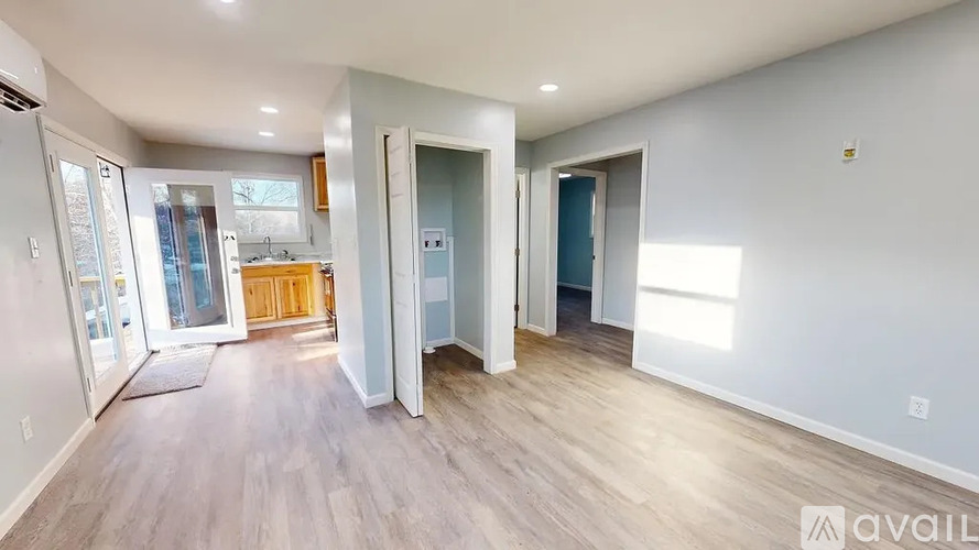 A spacious living room with a kitchen in the background and a doorway leading to another room.