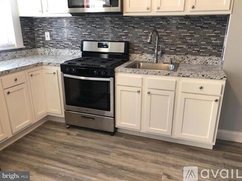 A kitchen with a black stove top oven and a sink with a granite countertop.