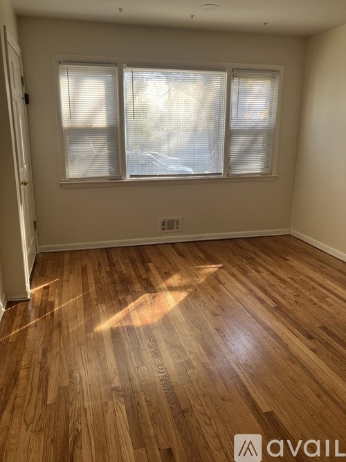 A room with wooden flooring and two windows.