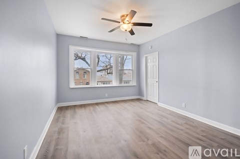 A room with a ceiling fan and a window showing a view of a house.